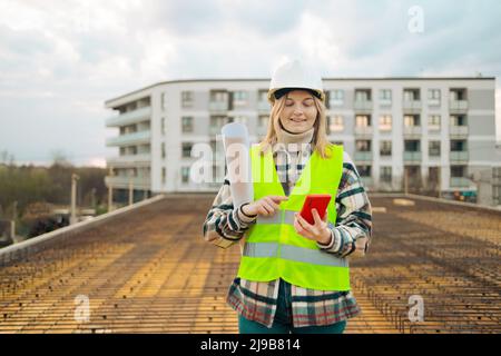 Female construction worker wearing uniform and safety helmet under inspection and checking construction by phone. Industry concept Stock Photo