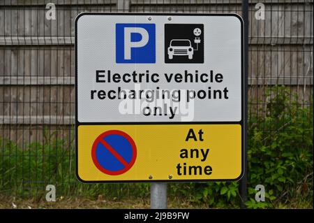 Electric vehicle recharging point sign UK, isolated against grass and wooden fence background Stock Photo