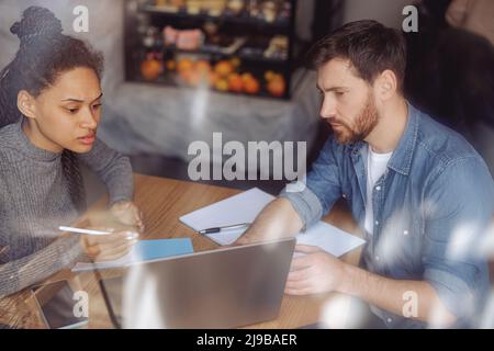 Hard-working man and woman sturtupers sitting at table in cafeteria and discussing project. Stock Photo