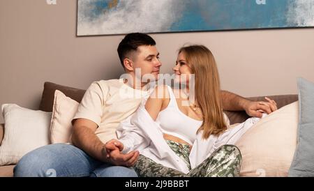 Happy love couple relaxing on sofa at home, sitting and looking at each other. High quality photo Stock Photo