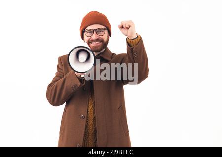 It's time for sales. Studio shot of a hipster millennial man in brown autumn outwear holding loudspeaker and throwing his fist in the air over white background. High quality photo Stock Photo