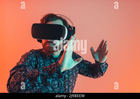 Studio shot of a professional gamer in patterned shirt wearing virtual reality VR goggles set playing video game. Copy space. High quality photo Stock Photo