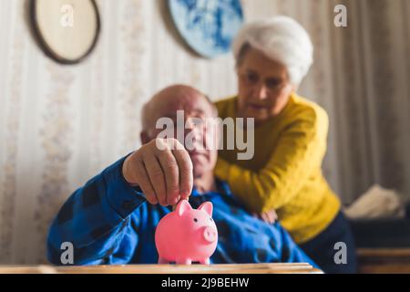 senior couple saving money in piggybank at home medium shot indoor financial problem concept. High quality photo Stock Photo