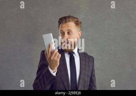 Businessman in suit looking at mobile phone with happy surprised face expression Stock Photo
