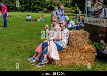 Two ladies drink a coffee sitting on a bale of hay on the first day of the Autumn Harrogate Flower Show at Newby Hall in Ripon in England. Stock Photo