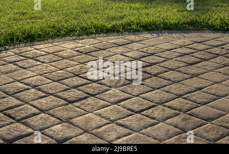 Stamped concrete pavement cobblestones pattern, decorative appearance of paving cobblestones tile on cement flooring in a park with green lawn Stock Photo