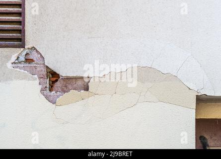 Damaged building facade is falling, visible bricks on the wall are behind broken fissured surfaces of concrete Stock Photo