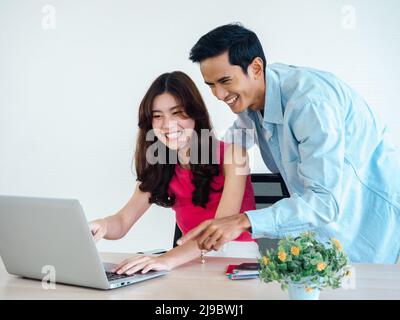 Happy Asian couple, young man and woman using tablet and laptop computer together for flight booking, hotel room and trip information at home, ready t Stock Photo