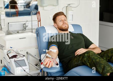 Portrait of military man giving blood while laying in chair at blood donation center, copy space Stock Photo