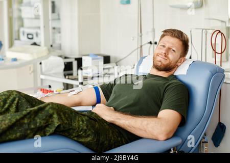 Portrait of military man giving blood while laying in chair at blood donation center and smiling at camera, copy space Stock Photo