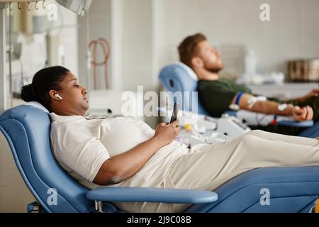 Side view portrait of two people giving blood and lying in chairs at donation center, copy space Stock Photo