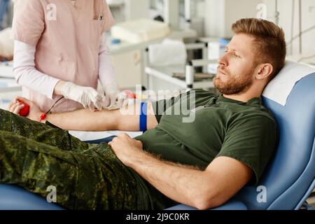 Portrait of male soldier giving blood at donor center with nurse helping, copy space Stock Photo