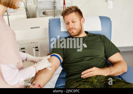 Portrait of young military man giving blood at donor center with nurse helping, copy space Stock Photo