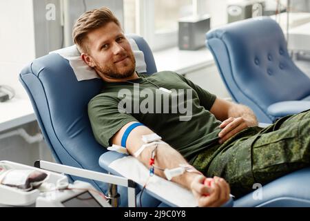 Portrait of smiling young man giving blood at donor center in comfort while lying in chair, copy space Stock Photo