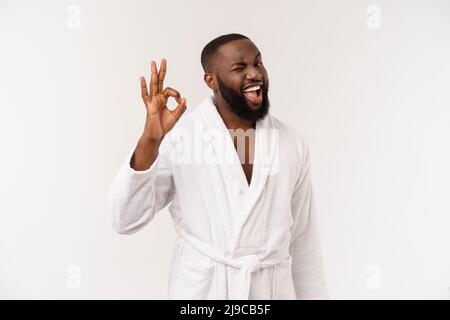 Young African man in bathrobe prepare for skin care showing ok finger sign. Human emotions concept Stock Photo