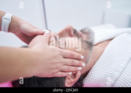Close up of man getting facial massage and relaxing with eyes closed at spa Stock Photo