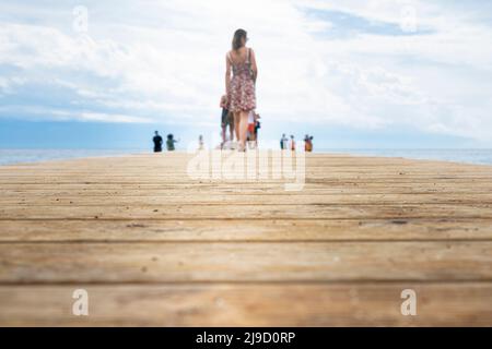 Wooden pier. Boardwalk at sea shore with beautiful woman and people in the distance. Focus on the wooden boards Stock Photo