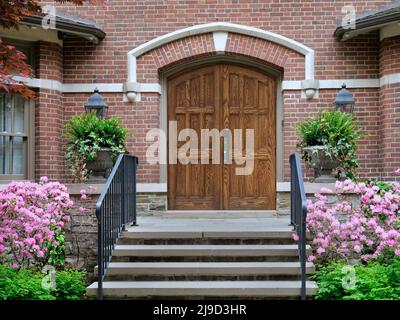 House entrance with elegant double wooden front door and flowering azalea bush Stock Photo