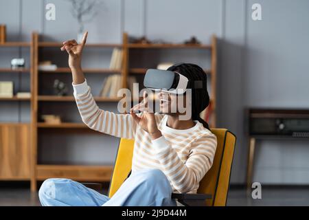 Excited african woman leaning on chair wearing vr headset playing in virtual games during work break Stock Photo