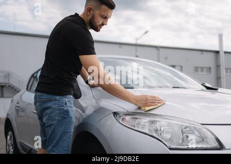 Hand of man wipes headlight of his car using rug. Self-service car wash. Outdoor Stock Photo