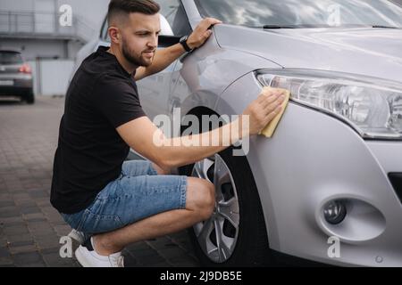 Hand of man wipes headlight of his car using rug. Self-service car wash. Outdoor Stock Photo