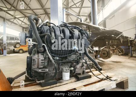 Passenger car engine in the foreground ready for installation, and cars in the background at shallow depth of field in a car service Stock Photo
