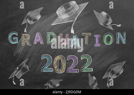 Hand drawn text GRADUATION 2022 and graduation caps on blackboard. Stock Photo