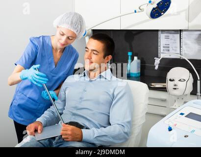 Female cosmetician explaining man hardware facial procedure in ...