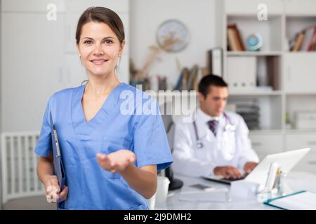 Female doctor making welcome gesture, politely inviting patient in office Stock Photo