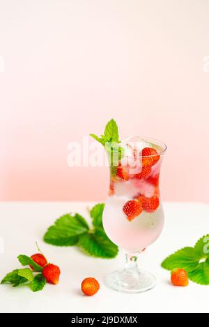 Strawberry drink.Refreshing summer cocktail.Summer drink.mineral water glass with ice and strawberries and strawberries with leaves on a light pink Stock Photo
