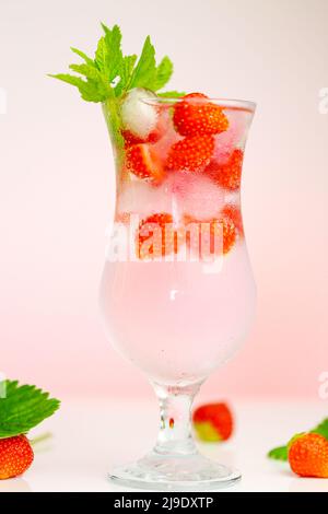 Strawberry drink.Refreshing summer cocktail.Summer drink.mineral water glass with ice and strawberries with leaves on a light pink background.Drink Stock Photo