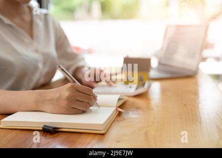 Close up real estate agent working with calculator taking note for financial loan on wooden desk Stock Photo