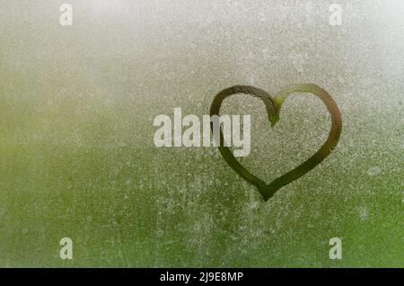 Heart painted on window which fogged up after rain with blurred green color background. Stock Photo