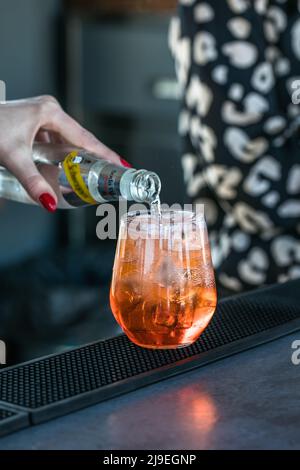 Expert barwoman is making cocktail at night club or bar. Orange juice fresh cocktail drink in hand. Alcoholic, non-alcoholic drink-beverage at the bar Stock Photo