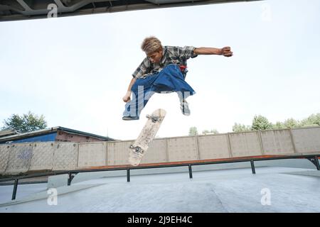 Portrait of teenage boy doing skateboard tricks in air at outdoor skatepark in urban area Stock Photo