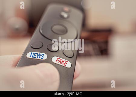 TV remote in hand with inscriptions on the buttons fake and news. The inscription fake in red and the inscription news in blue on the buttons of the T Stock Photo