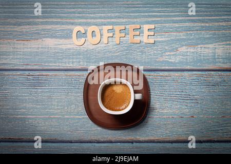 Brown tasty coffee drink served on a white cup with brown plate on a blue wooden table and coffee word Stock Photo