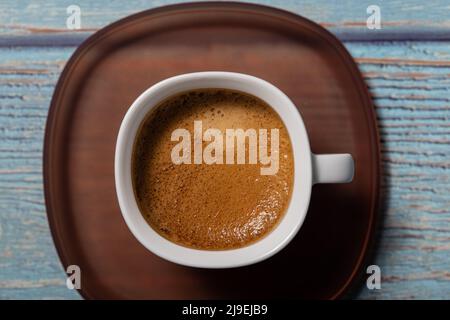 Brown tasty coffee drink served on a white cup with brown plate on a blue wooden table Stock Photo
