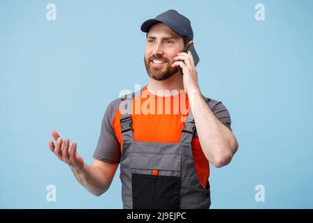 Delivery employee man in uniform talk on mobile phone on blue studio background Stock Photo