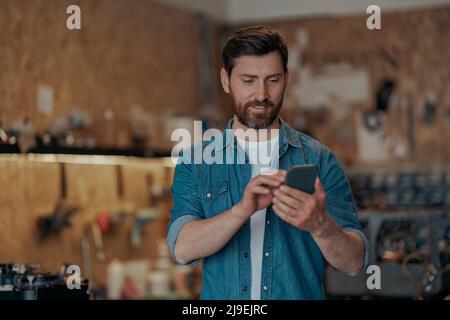 Male worker using phone standing in own workshop Stock Photo