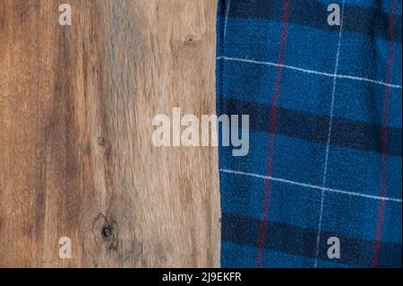 The blue checkered fabric lies against the wooden background. A towel or kitchen napkin on the rough boards or kitchen table. Stock Photo