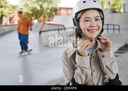 Portrait of smiling young girl wearing protective guards and helmet in skatepark, copy space Stock Photo