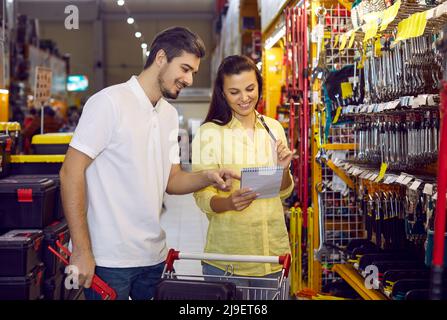 Young married couple in a home goods store. A woman holds a list on paper in her hands for choosing various tools for home repairs and other work. Stock Photo