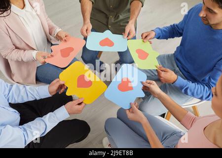 Young people sitting in circle and holding colored speech bubbles with red hearts on them. Stock Photo