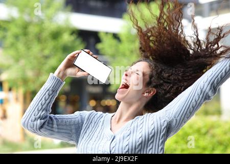 Happy woman singing in the street showing blank phone screen Stock Photo