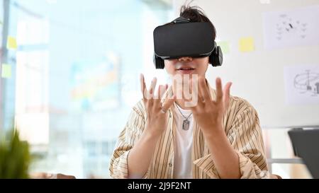 An intelligent Asian male wearing VR glasses, trying modern virtual experience with VR glasses in the office. Stock Photo