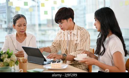 Smart Asian young male software engineer working with senior female product manager and young female assistant in the office. Stock Photo