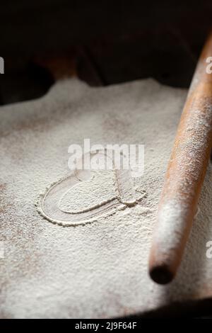 A heart is drawn on a cutting board sprinkled with flour. Next to the rolling pin for dough Stock Photo
