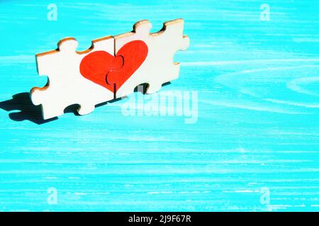 Heart symbol made from two matching jigsaw puzzle pieces on a blue wooden background. Creative romantic concept. Stock Photo