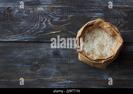 Raw white long-grain basmati rice in a craft bag on a wooden background, top view, space Stock Photo